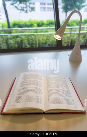 Vertical view mood shot of a open book on table with a LED reading lamp. Singapore. Stock Photo