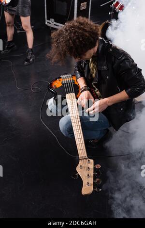 KYIV, UKRAINE - AUGUST 25, 2020: Overhead view of curly musician squatting with electric guitar on knees during rock band rehearsal Stock Photo