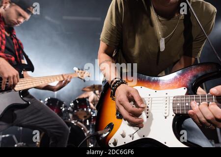 KYIV, UKRAINE - AUGUST 25, 2020: Rock band musician leaning and playing electric guitar with pick with blurred musicians on background Stock Photo