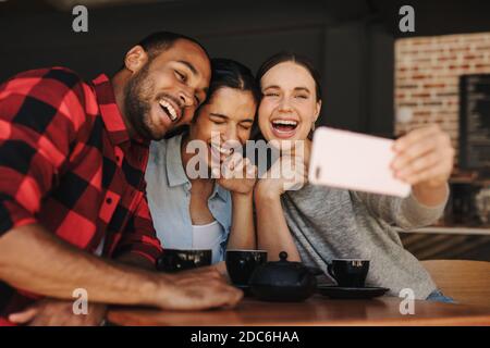 Woman taking selfie with friends in a cafe. Friends in coffee shop having fun and taking selfies. Stock Photo
