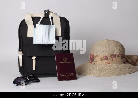 A view of black backpack with passport, hat, and mask on white background - travel concept Stock Photo