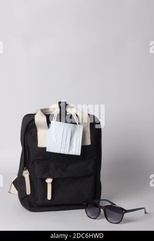 A vertical shot of black backpack with sunglasses, and mask on white background - travel concept Stock Photo