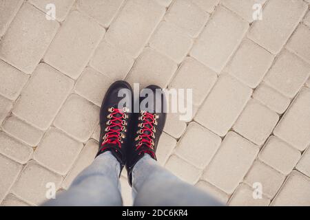 Top above high angle first person view cropped photo of girl legs wear black leather boots shoes with red lace on stone road Stock Photo