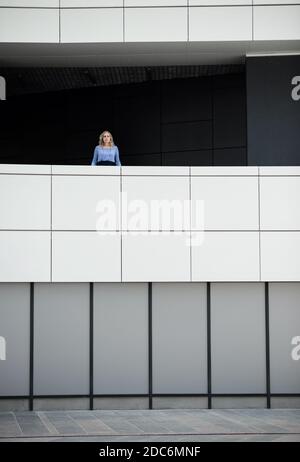 Blond woman is standing on a balcony in a modern building Stock Photo