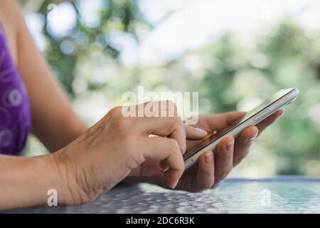 Woman's hands holding smartphone, glass table in outdoor cafe Stock Photo