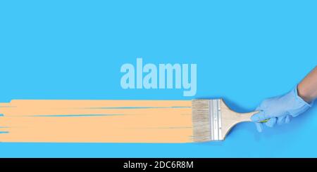 Brush for paint in hand on a blue background. Paint brush with wooden handle of a human hand with copy space. Long wide banner Stock Photo