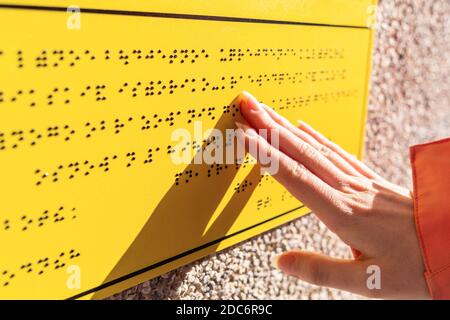 Blindness. A woman reads a yellow Braille sign. Close up of hands. Concept of the day of the blind and disability. Stock Photo