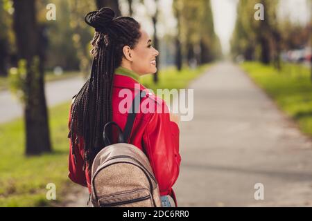 Back rear view photo of young attractive african woman happy positive smile walk street tourism hold backpack look empty space Stock Photo