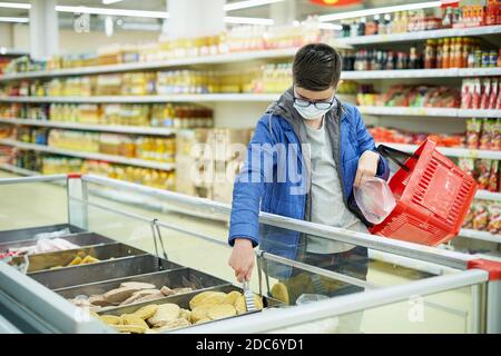 Boy Teenager in protective mask buys frozen food at the grocery store Stock Photo