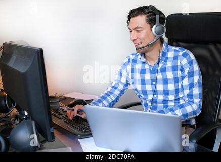Man with headset in a video call - working from home with a laptop in the living room Stock Photo