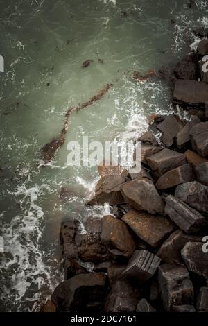 rocks crashing on the shore against rocks or sea defences shot from above Stock Photo