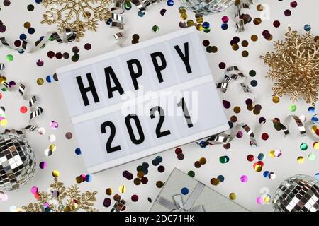 lightbox with words happy 2021, gift box, disco balls, snowflakes and holiday confetti on white background. top view. Happy New Year 2021 concept.  Stock Photo