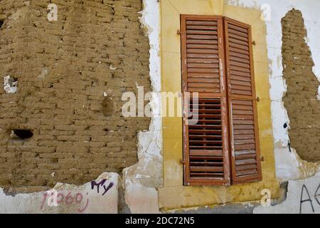 Old handmade clay and straw mud bricks exposed in house wall with shuttered dressed stone surround of window Stock Photo