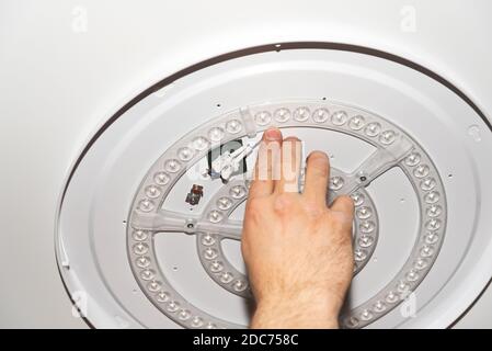 LED lamp on the ceiling a man's hand holds in the middle on a light background Stock Photo