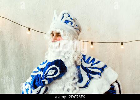 Santa Claus in a blue fur coat looks out the window, thinks and touches his beard. Stock Photo