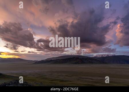 Steppe of Mongolia with dark colored clouds and mountains during sunset. Stock Photo