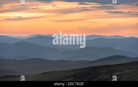 Steppe of Mongolia with colored orange clouds and mountains during sunset. Stock Photo