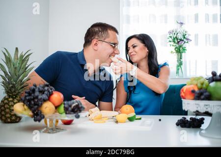 Happy married couple eating fruits. Wife feeding husband with banana. Healthy activity, indoors, cold prevention Stock Photo