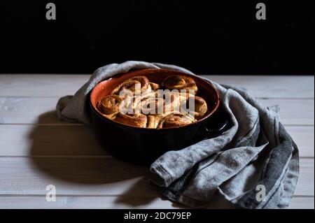 cinnamon buns on a white wooden background in an oven dish with a grey towel to take out of the oven Stock Photo