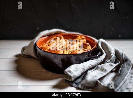 cinnamon buns on a white wooden background in an oven dish with a grey towel to take out of the oven Stock Photo