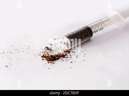 Creative concept of a coffee shot, ground coffee in a plastic syringe on white background with coffee powder splash and two roasted black coffee beans Stock Photo