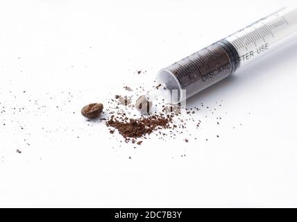 Creative concept of a coffee shot, ground coffee in a plastic syringe on white background with coffee powder splash and two roasted black coffee beans Stock Photo