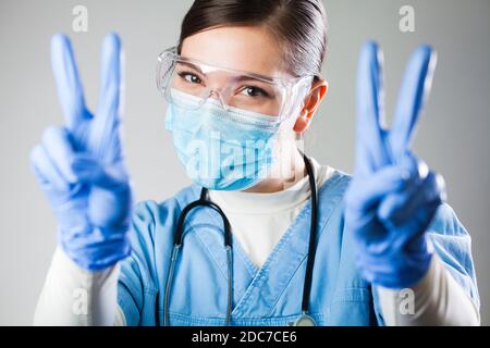 Attractive female caucasian doctor in uniform and protective personal equipment smiling and showing V sign symbol,Coronavirus COVID-19 virus disease Stock Photo