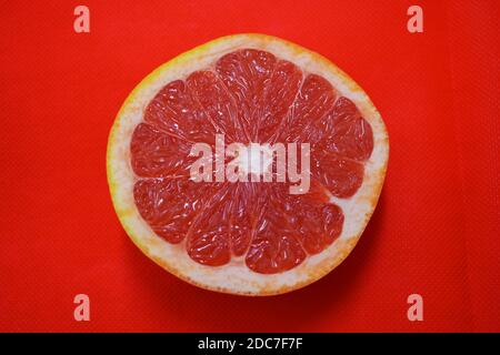 Halves of ripe juicy grapefruit, divided in half, placed on a red fabric background. Delicious and healthy sweet and sour fruits for the human body. Stock Photo