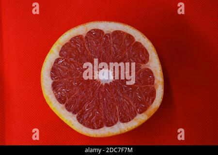 Halves of ripe juicy grapefruit, divided in half, placed on a red fabric background. Delicious and healthy sweet and sour fruits for the human body. Stock Photo