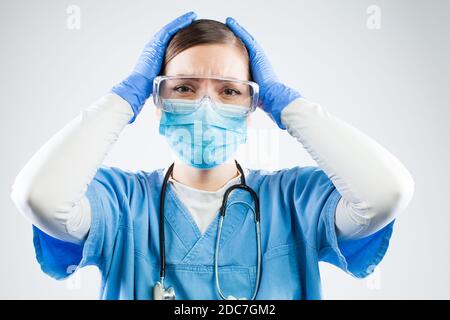 Desperate female doctor,hands on head,worried terrified and devastated medical professional,tragic circumstances leading to numerous dead patients and Stock Photo