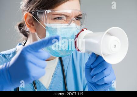 Angry doctor in blue uniform yelling orders and commands over megaphone, medic handling staff and patients in quarantine or emergency situation,Corona Stock Photo
