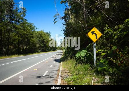 Turn right road sign along the empty highway road in Chile. Warning road sign with black arrow on yellow background along bicycle lane. Stock Photo