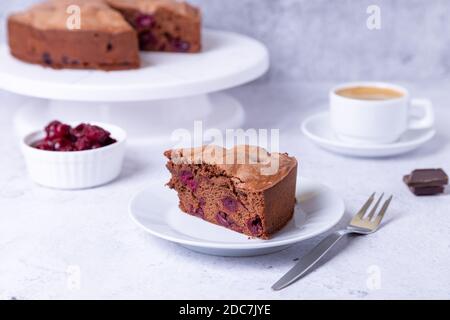 Chocolate cherry pie on a white plate. In the background is a pie, a cup of coffee, cherries and pieces of chocolate. Stock Photo
