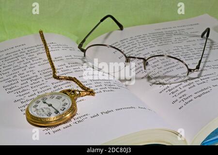A man's gold pocket watch and chain lying on a copy of Winnie the Pooh. Stock Photo