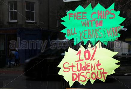 Free chips with kebabs and wraps with a 10% student discount sign, in a Fish and Chip shop window, UK Stock Photo