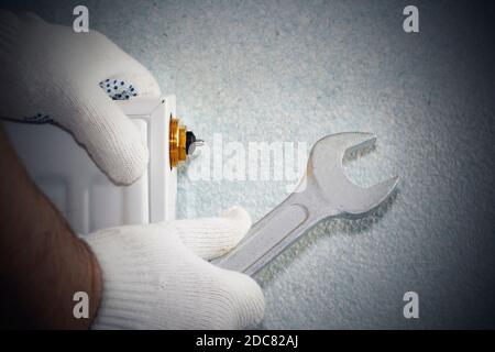 Man is repairing radiator battery in the room. Maintenance repair works renovation in the flat. Heating restoration. Wrench in hands. Stock Photo