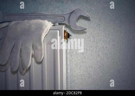 Man is repairing radiator battery in the room. Maintenance repair works renovation in the flat. Heating restoration. Wrench in hands. Stock Photo
