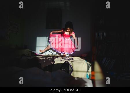 A little girl in a bright costume dances in a light patch in dark room Stock Photo