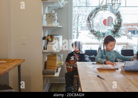 Two children sit together in kitchen creating music and art by window Stock Photo