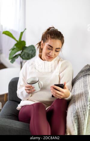 Woman holds mug while checking her phone Stock Photo