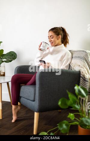 Woman holds mug while checking her phone Stock Photo