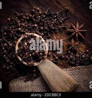 Top view composition with aromatic dried clove buds in wooden spoon placed on table with scattered star anise and clove spices Stock Photo