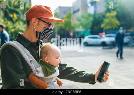 Father with baby daughter video calling through smart phone on street during COVID-19 Stock Photo