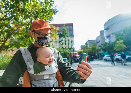 Man with happy baby daughter video calling through smart phone while sitting on bench in city during COVID-19 Stock Photo