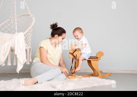 Tender Mom And Son. Child Sitting On Ride On Toy In Playroom. Toddler Baby Boy Riding Swinging On Rocking Chair Toy Horse. Stock Photo