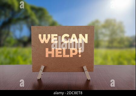 We can help card on the table with sunny green park background. Stock Photo