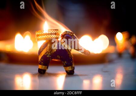small elephant incense holder with smoke coming out and an out fo focus background with diya oil lamps lit behind it with flickering flames Stock Photo