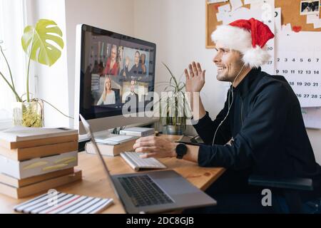 Virtual Christmas day house party. Man smiling wearing Santa hat Business video conferencing Young man having video call via computer in the home xmas Stock Photo
