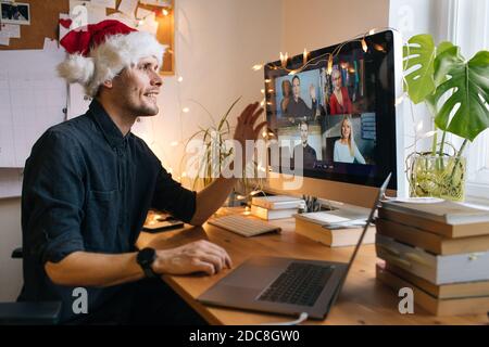 Virtual Christmas day house party. Man smiling wearing Santa hat Business video conferencing Young man having video call via computer in the home xmas Stock Photo