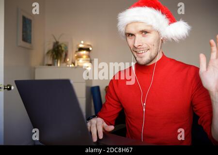 A video call on Christmas computer in the home office. Man wearing Santa hat. Business video conferencing. Virtual thanksgiving house party. Online Stock Photo
